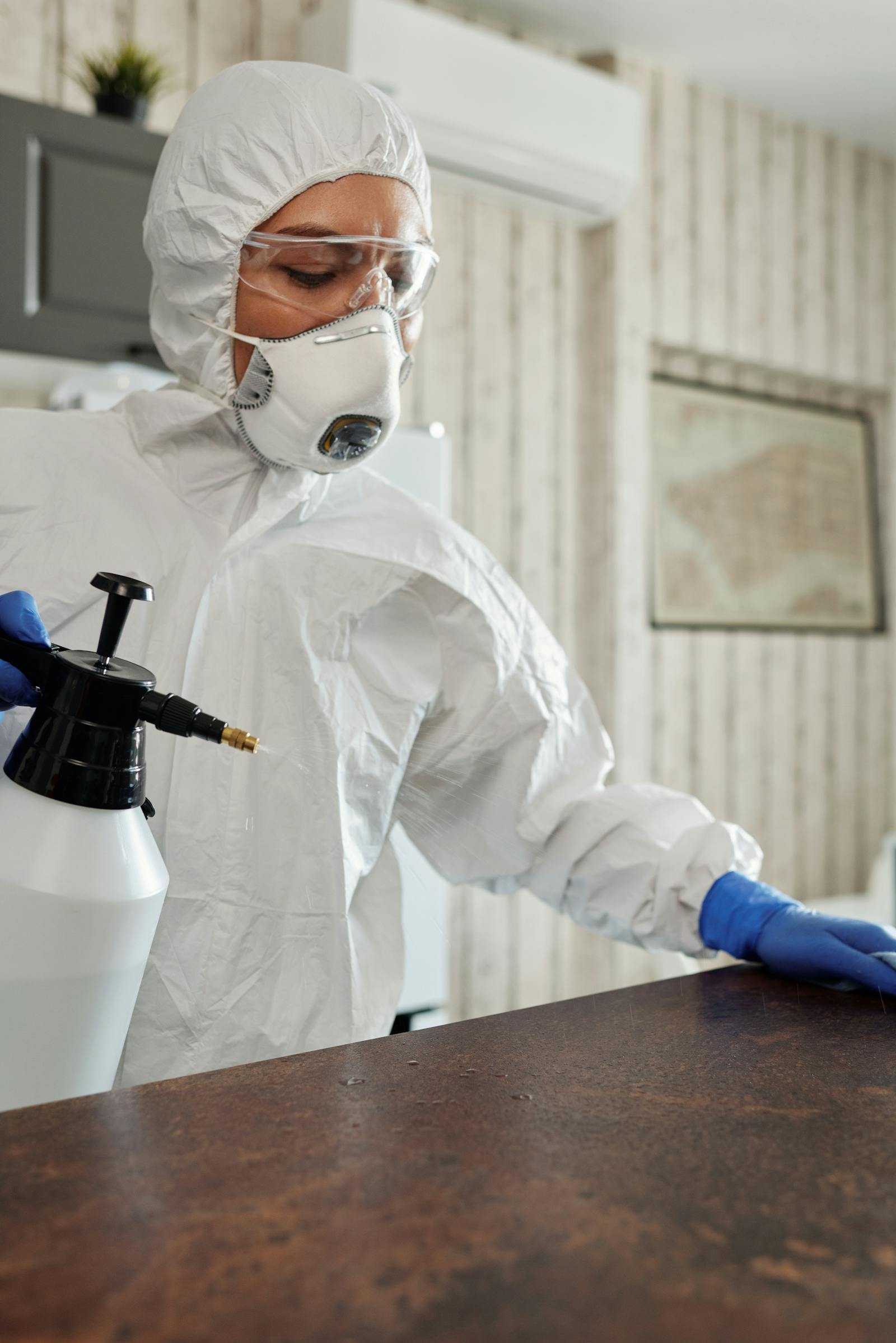 Protective worker spraying disinfectant across an indoor surface